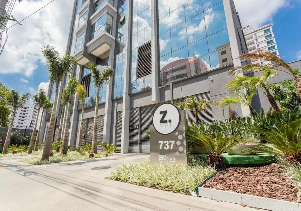 Vista do prédio espelhado do Studios Sampa - Moema Cotovia. Há um jardim na frente e várias árvores plantadas. Foto para ilustrar o post sobre hotéis em Moema.