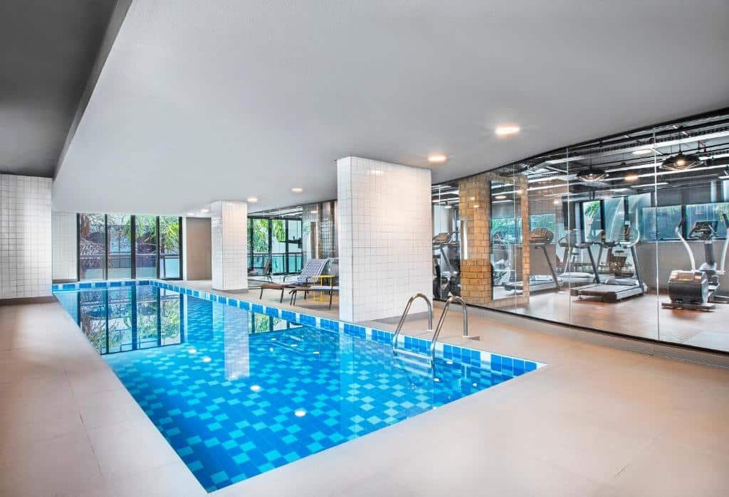 Área interna de piscina e academia no Meliá Ibirapuera. As áreas são separadas por uma parede de vidro. Ambas são cobertas. Há espreguiçadeiras perto da piscina, e uma escada para entrar na mesma. Imagem para representar o post sobre hotéis em Moema.