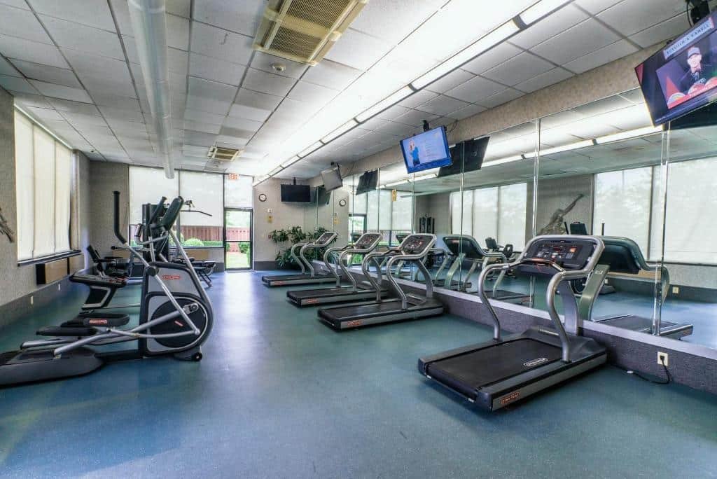 Imagem de uma academia no Holiday Inn Newark International Airport. O espaço é equipado com uma variedade de equipamentos de exercícios, incluindo esteiras, bicicletas ergométricas, máquinas de musculação e pesos livres. Há também espelhos ao longo das paredes e uma área dedicada para alongamento.