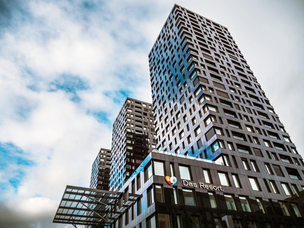 Prédio do cinza e com várias janelas espelhadas do aja Zürich, um dos hotéis em Zurique, com céu azul e nuvens brancas