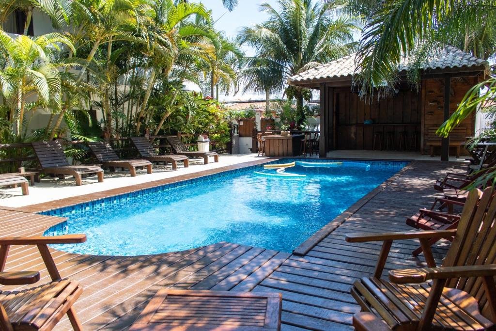 Piscina ao ar livre no Arco Íris Pousada, com macarrões de piscina dentro, ao redor cadeiras de tomar sol e árvores.