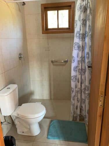 Banheiro do Celeiro das Águas Brancas, um dos chalés em Urubici, em que é possível algumas adaptações para PcDs, como barra de apoio no chuveiro, cortina de separação, evitando vidros, e vaso sanitário elevado.