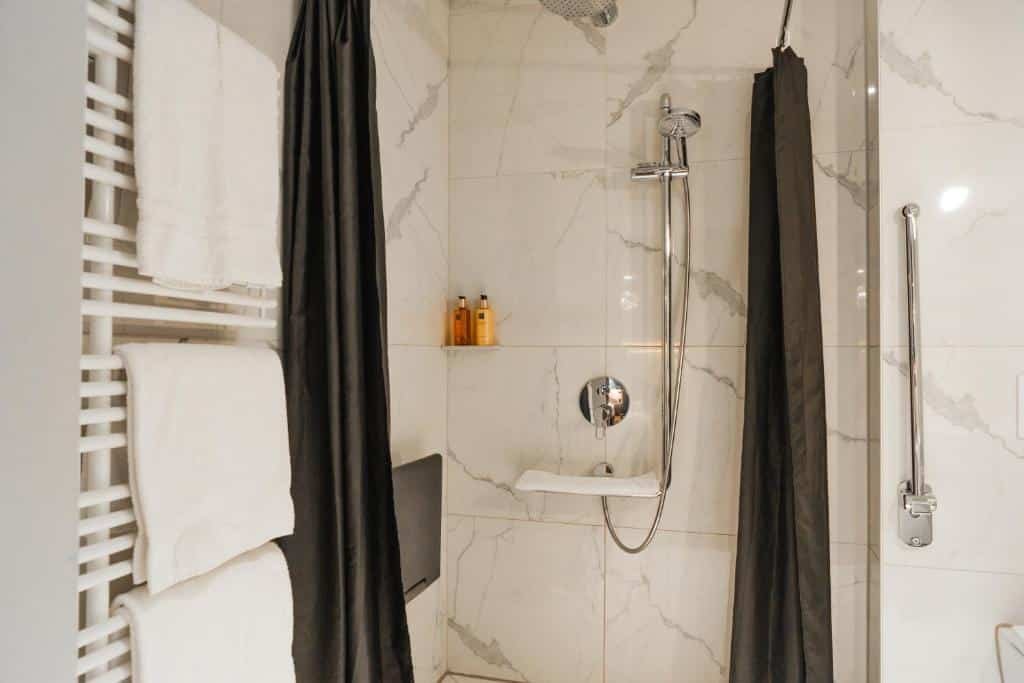 Banheiro com acessibilidade do Boutique Hotel Glacier com chuveiro do lado esquerdo e do lado direito uma barra de apoio.