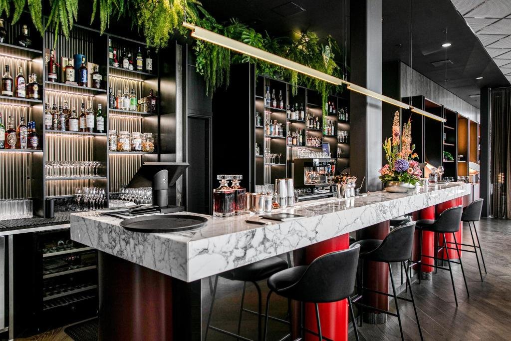 Bar do Clarion Hotel Oslo com balção de mármores, cadeiras pretas e bebidas na frente.