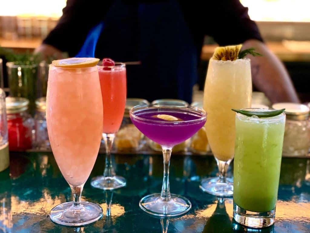 cinco drinques coloridos no bar do Pod Times Square, atrás do balcão é possível ver um homem branco com os braços apoiados na mesa.