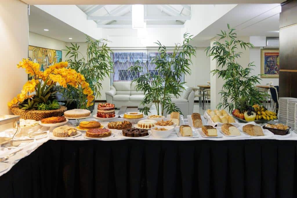 mesa de café da manhã do Le Village Flats Hotel e Business em Joinville com vários bolos e vários pães.