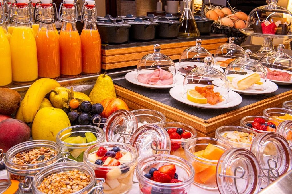 Uma foto de um buffet de café da manhã no Les Armures. Vemos várias coisas espalhadas na mesa, como frutas, geleias, sucos, temperos, frios, cereais, etc,
