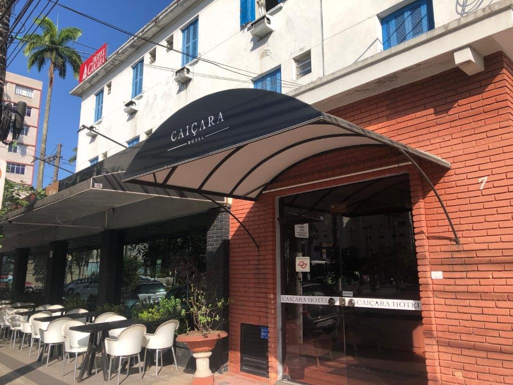 Fachada do Caiçara Hotel com uma parede de tijolinhos e uma maquise preta com o nome do hotel