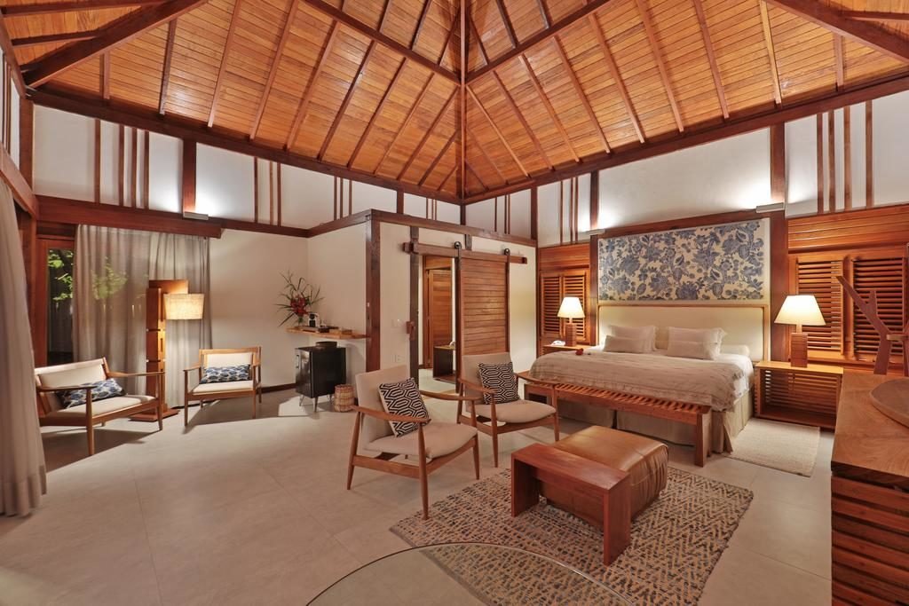 Quarto Camurim Grande, com cama e casal, cadeiras de madeira com almofadas, e uma decoração composta por lustres e móveis de madeira