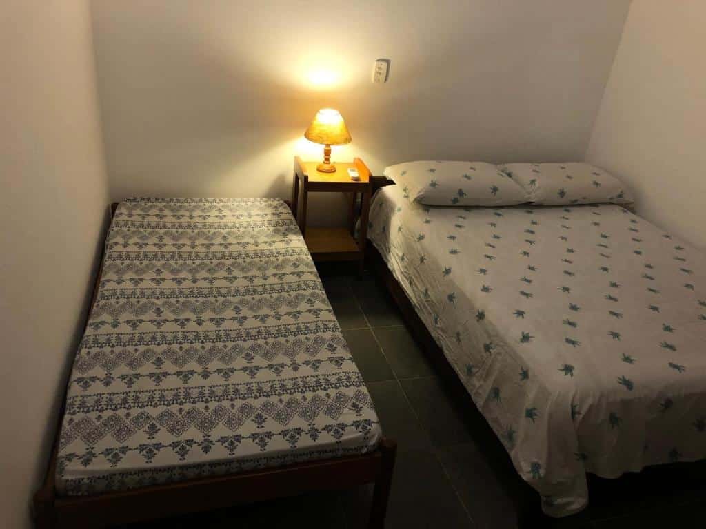 Foto do quarto no Residencial Marina Del Sol. Representa o post sobre airbnb em Paúba. Há uma cama de casal à direita e uma de solteiro à esquerda, e entre elas há uma mesa de cabeceira com abajur em cima.