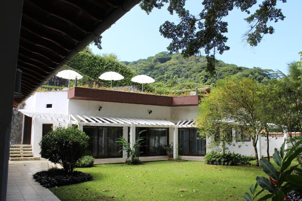 Acomodações em Casa da Uba Una, um enorme jardim, muitas árvores e arbustos, a casa é branca e as portas da varanda são de vidro