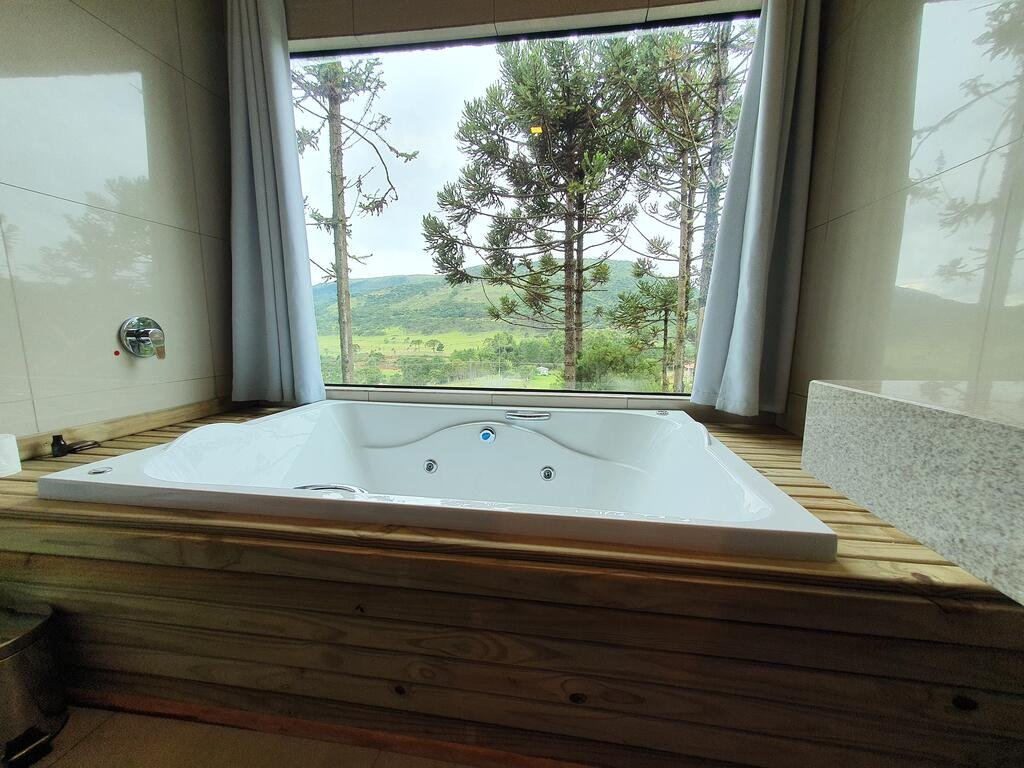 Banheira do Cascata dos Amores em um deck de madeira com janela de vidro acima que dá vista para araucárias.
