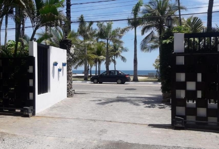 Entrada do Chalé Recanto do Barão. O portão fica do outro lado da rua da praia, sendo possível ver o mar muito próximo.