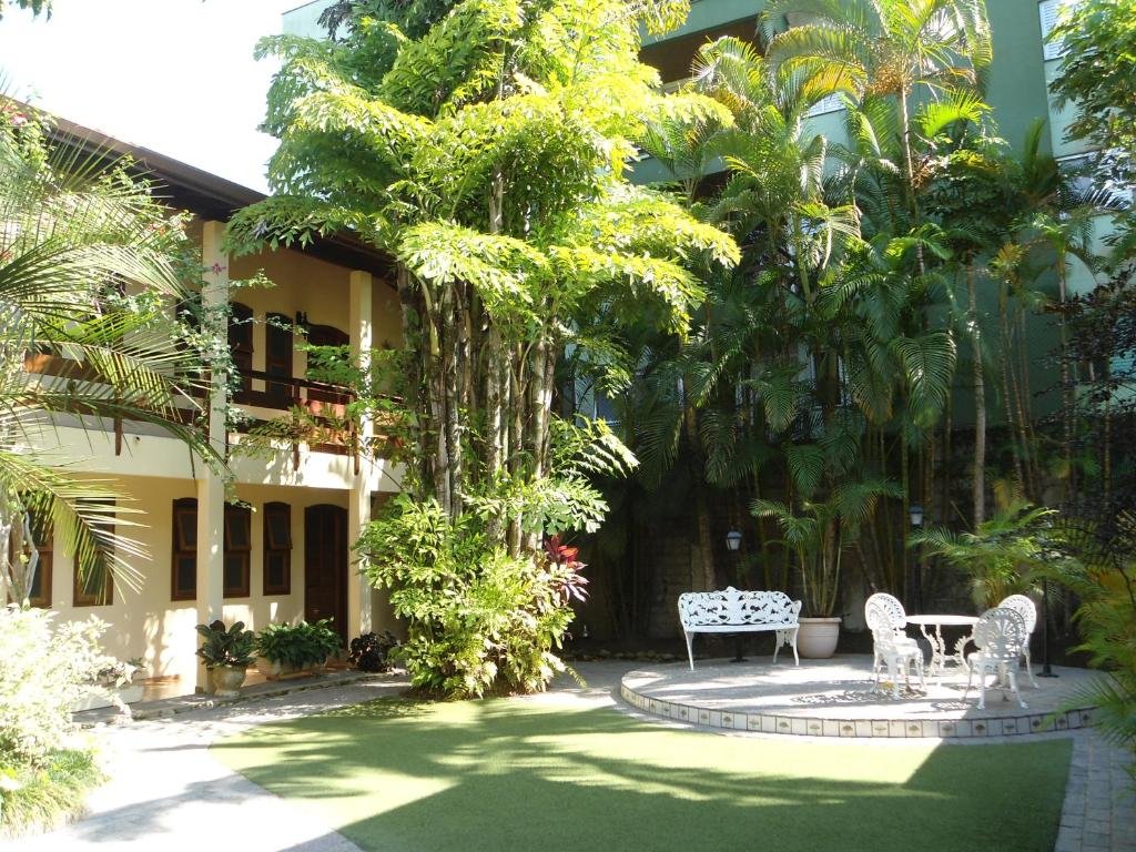 Parte externa do jardim em Chalés Estrela do Mar, um local com cadeiras para se sentar próximo da vegetação, algumas árvores e arbustos, ao lado, é possível ver os chalés em tom de amarelo com portas e janelas em madeira