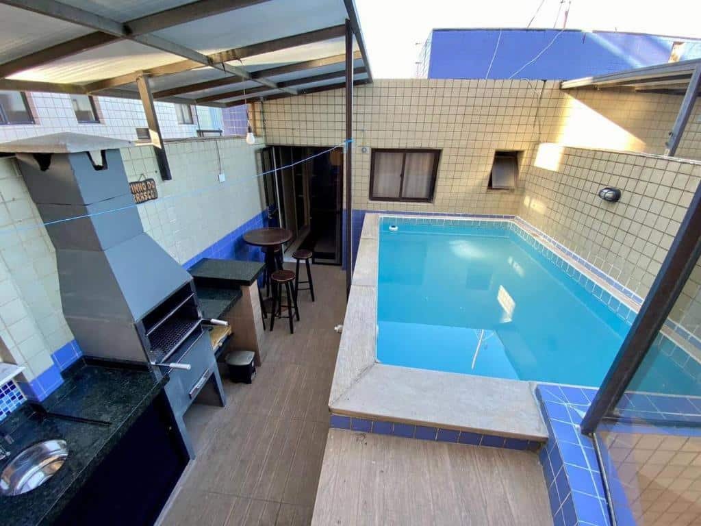 Cobertura de um prédio com piscina privativa azul no lado direito, pia, churrasqueira e pequena mesa redonda com bancos no lado esquerdo.