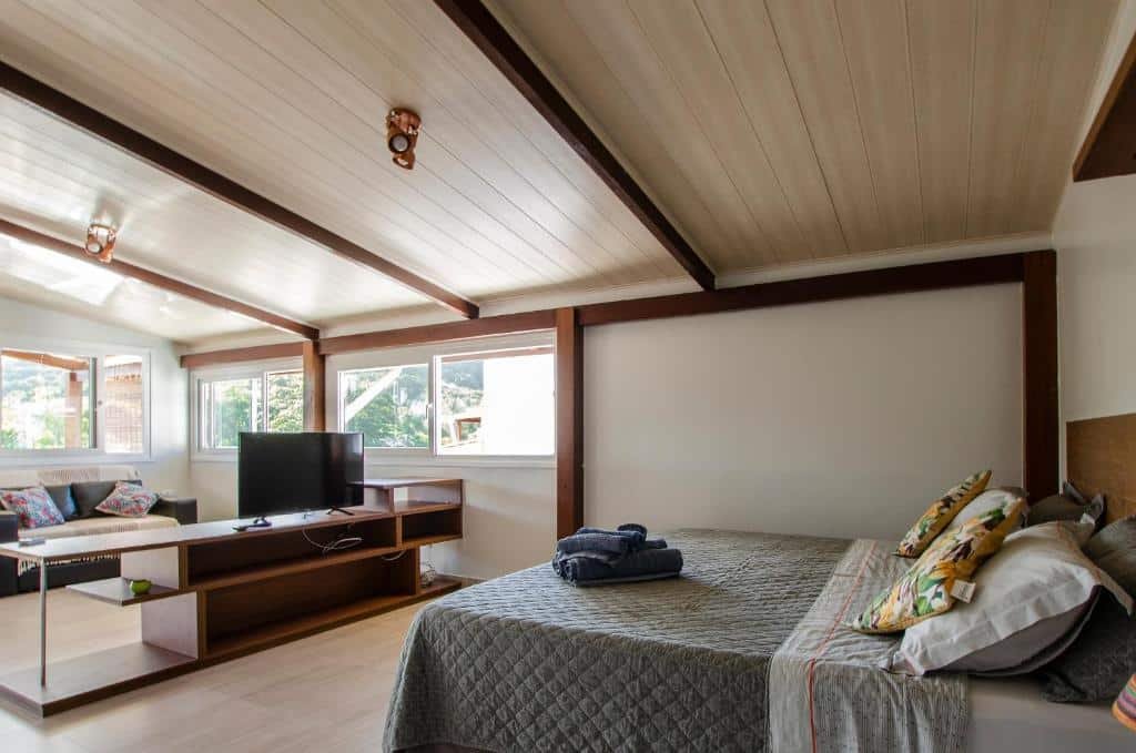 Quarto do Condominio Luna Rossa. Do lado direito uma cama de casal, no meio uma raque com uma televisão, no fundo, no lado esquerdo, um sofá. Foto para ilustrar post sobre airbnb em Morro de São Paulo.