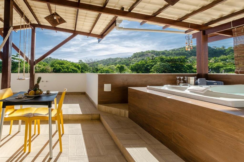 Área externa do Condominio Luna Rossa. Do lado direito uma banheira de hidromassagem. Do lado esquerdo uma mesa com cadeiras e uma fruteira em cima. No fundo um balanço e a vista de árvores.
