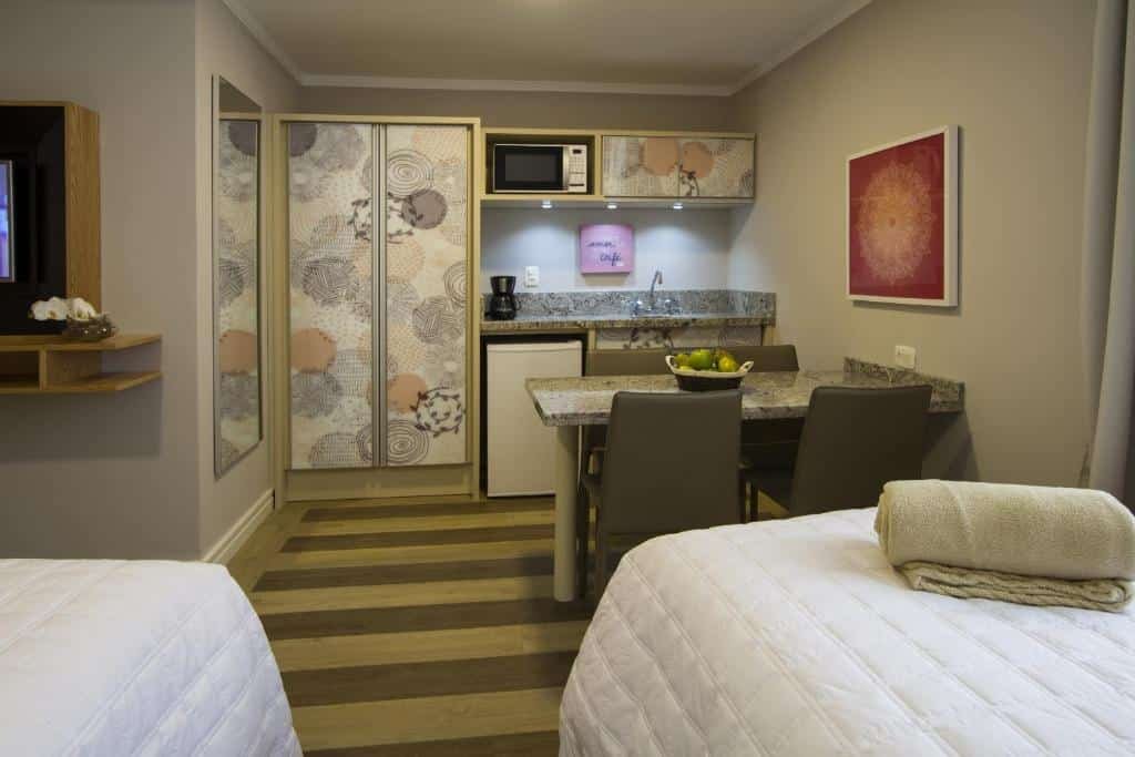 Mini cozinha do Rosa Flat Charm Gramado, com um balcão com 4 lugares, um frigobar, um armário e um micro-ondas