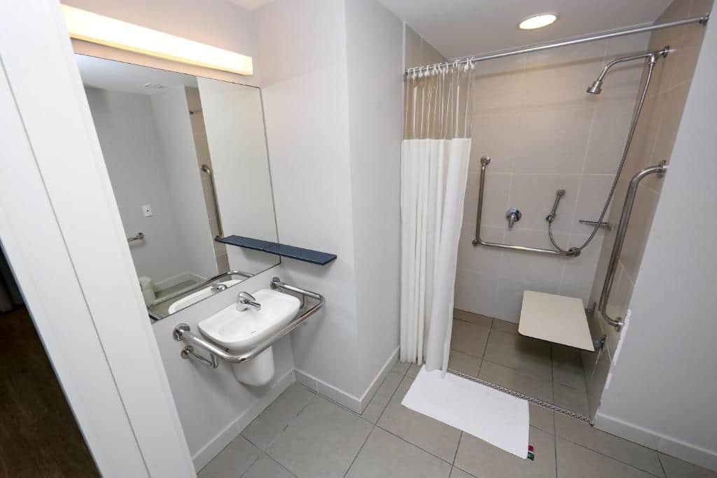 Banheiro adaptado do Delphin Surf Hotel com barras de apoio, box sem vidro com local para sentar-se e pia mais baixa