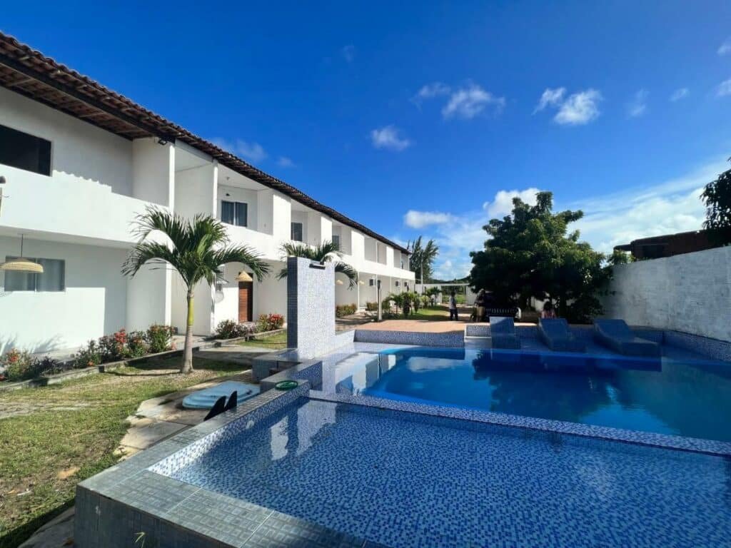 Piscina da Dlux Suites Baia Formosa. Ela é grande possui algumas divisões e três espreguiçadeiras. Há também uma cascata de água desligada. Em frente a ela está a propriedade.