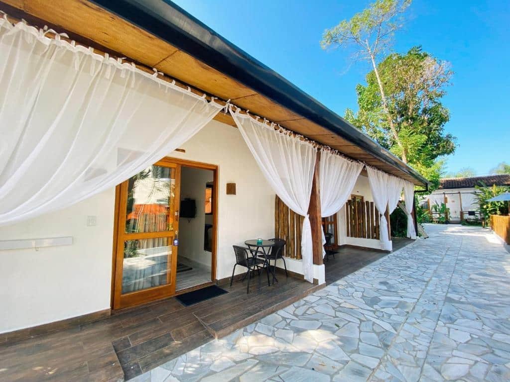 Entrada da Pousada Pono Village com várias janelas, com cadeiras perto das portas e cortinas brancas. Representa pousadas na praia do Engenho.