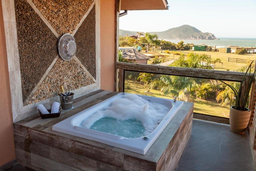 Hidro ao ar livre com bolhas de espuma em uma varanda com vista para uma colina pitoresca e para o mar, acompanhada de toalhas enroladas. Essa é a Fazenda do Rosa, um dos hotéis fazenda em Santa Catarina.
