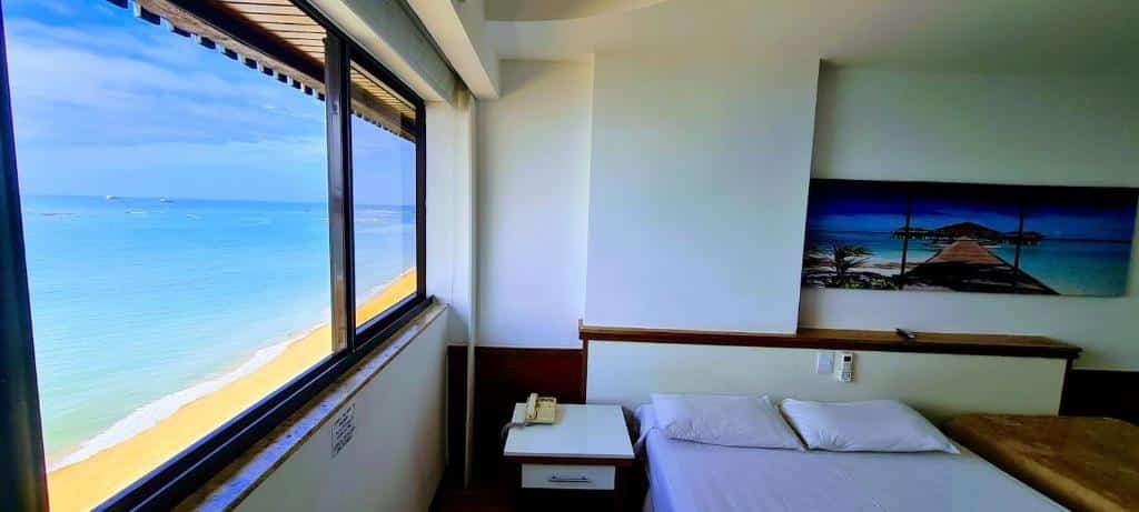 Quarto no Flat Pasárgada 906 com a janela dando vista direta para a praia, com uma cama de casal e uma de solteiro