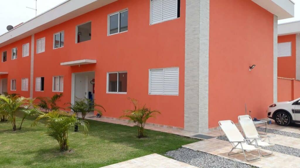 Frente do Apartamento Boracéia Bertioga durante o dia com jardim a frente e atrás o prédio. Representa airbnb na praia da Juréia.