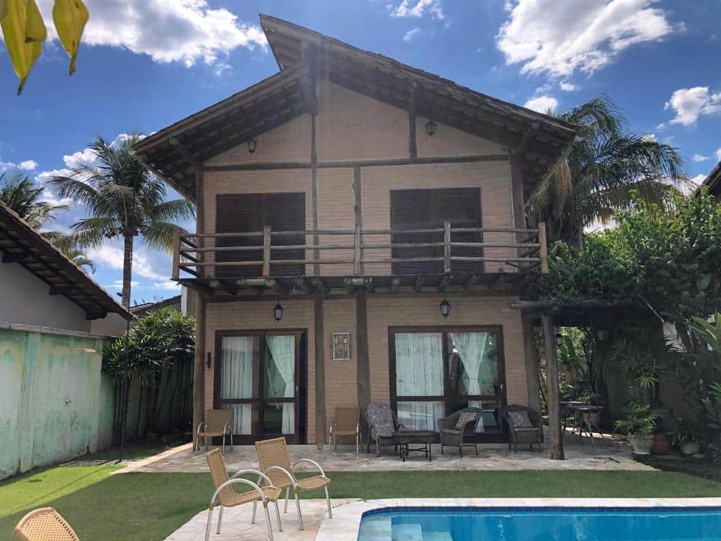 Frente da Casa com Piscina, Barra do Una durante o dia com piscina do lado direito da imagem a frente com duas cadeiras do lado esquerdo da imagem perto da piscina e ao fundo a propriedade.