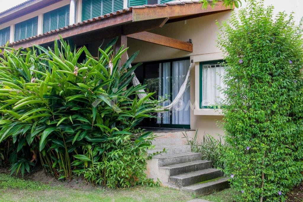 Frente da Casa em Condomínio na Praia em São Sebastião durante o dia com jardim a frente e ao fundo a propriedade.