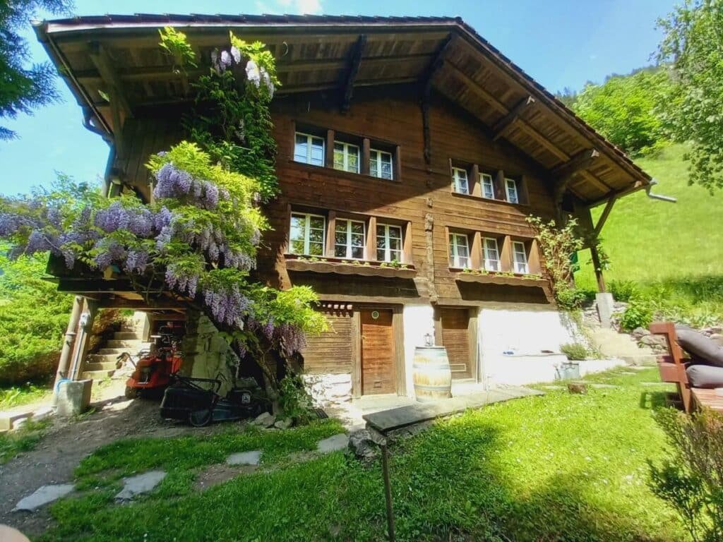 Imagem do Chalet Elza durante o dia com jardim em volta e no centro da imagem um chalé de madeira. Representa hotéis em Lauterbrunnen.