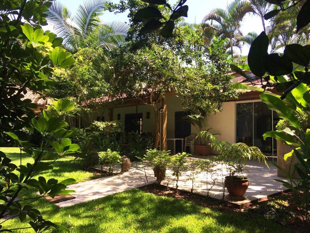 Frente da Juréia Dreams durante o dia com jardim a frente e do lado direito da imagem ao fundo a estadia. Representa airbnb na praia do Engenho.