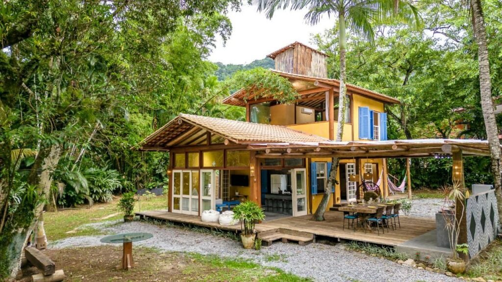 Frente da casa Nosso quintal é a praia de Maresias durante o dia com a estadia no centro e em volta árvores.