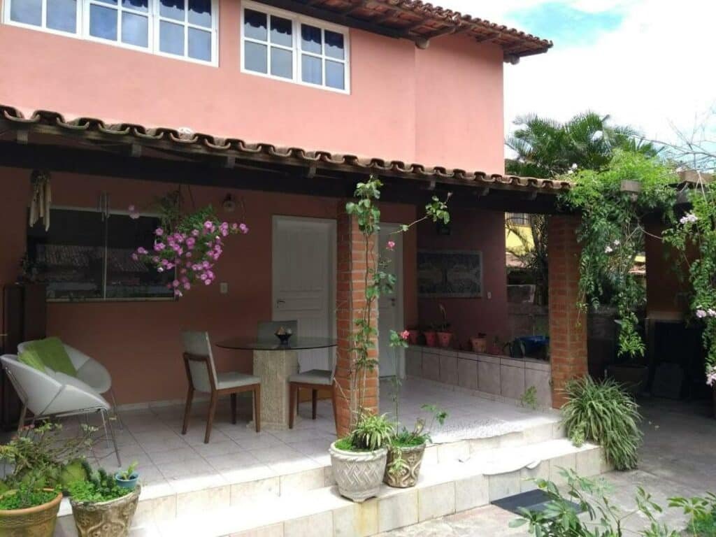 Varanda na Hospedaria Vila Else, uma cama com dois andares vermelha, uma varanda com plantas e flores, além de uma mesa e cadeiras