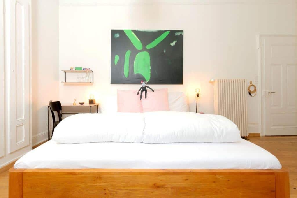 Foto do Hotel Beau Séjour Lucerne, para representar o post de hotéis em Lucerna. A cama do quarto é de casal e está centralizada na imagem. Há um macaquinho de pelúcia em cima dos travesseiros. Um quadro decora a parede atrás. Uma mesa com cadeira está na esquerda da cama. Ainda nesse lado também vemos parcialmente um guarda-roupa.
