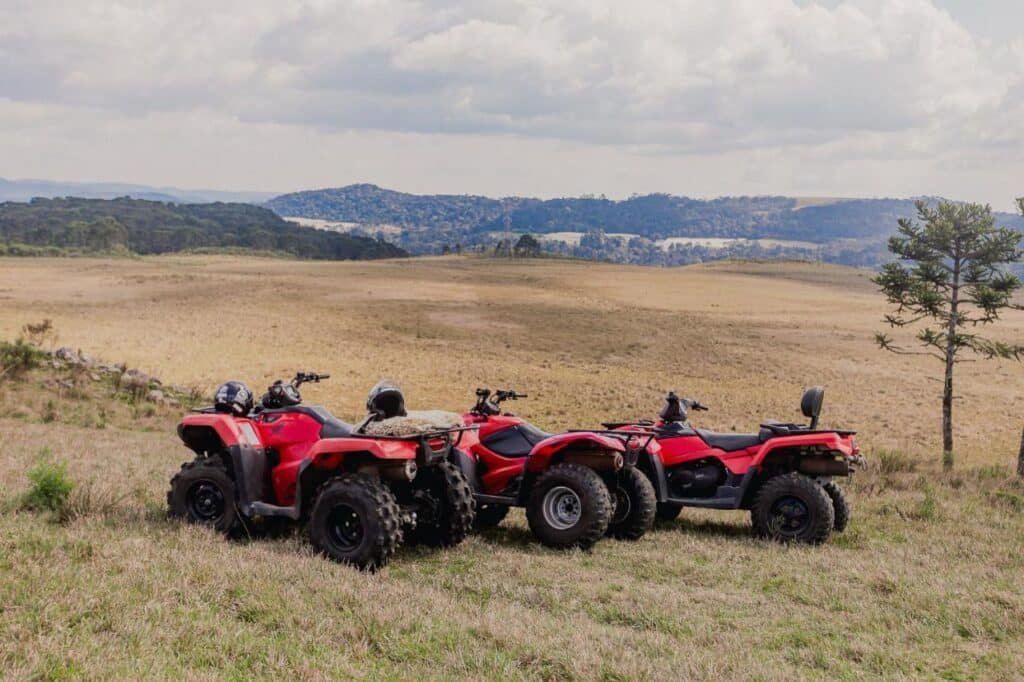 Três quadriciclos vermelhos estacionados em um campo gramado com uma paisagem cênica de colinas e árvores ao fundo no Hotel Fazenda Rota dos Cânions, um dos hotéis fazenda em Santa Catarina.
