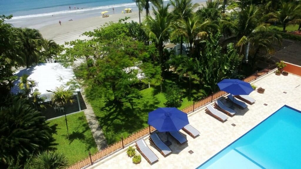 Vista aérea da parte da piscina e gramado do Hotel Porto Di Mare, logo em seguida, já é possível ver a Praia da Enseada em Ubatuba