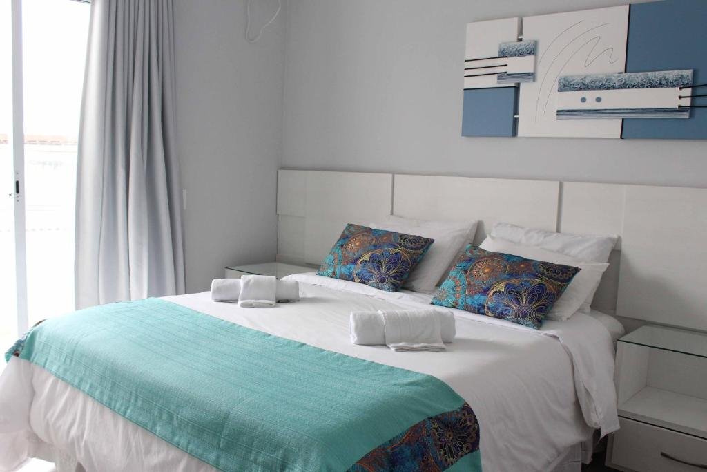 Quarto do Hotel Pousada da Néia. Uma cama de casal está no meio, com duas toalhas em cima. Ao seu lado há uma porta transparente com cortina. 