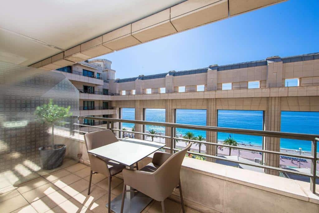 Área externa do Hyatt Regency Nice Palais de la Méditerranée. Varanda com uma mesa, duas cadeiras e vista para a praia em frente ao hotel.