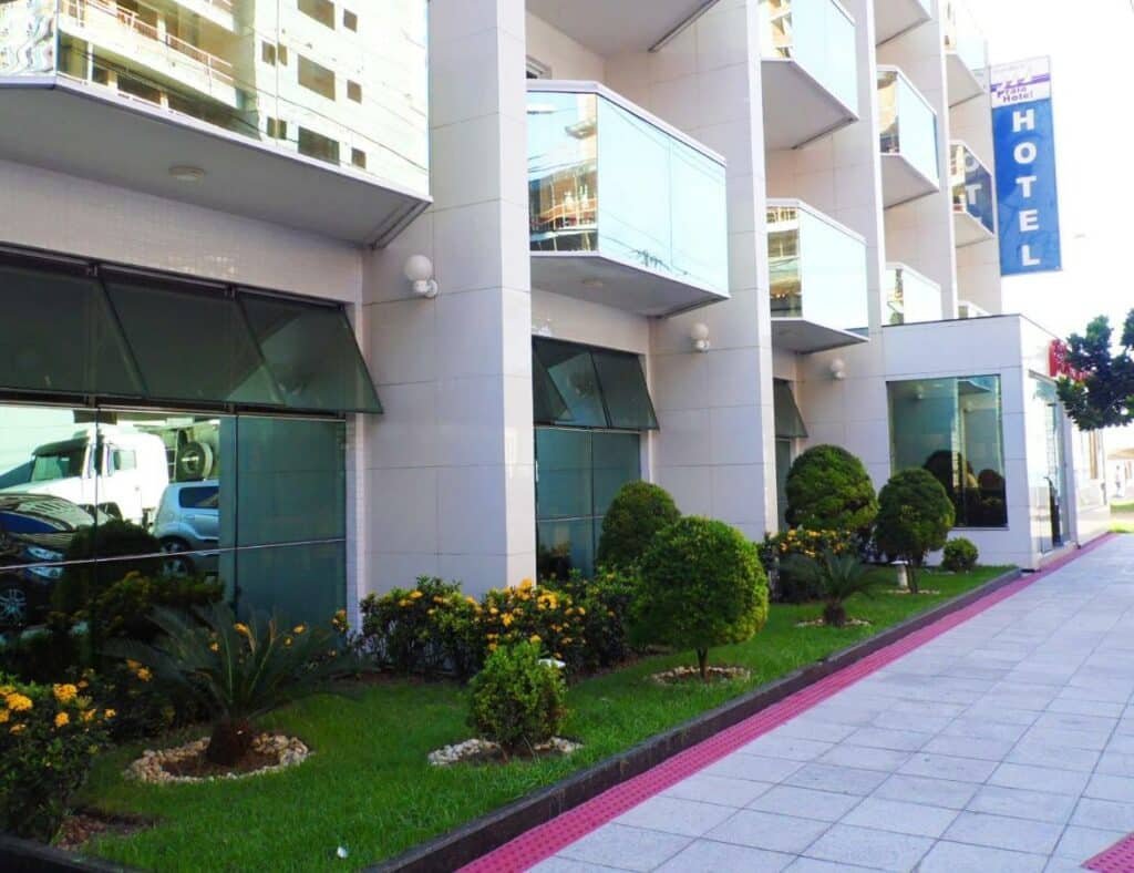 Entrada do Itaparica Praia Hotel com sacadas dos apartamentos e um gramado com arbustos e plantas