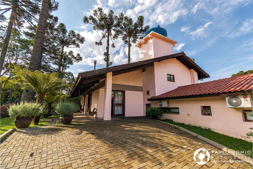 Exterior do Jardins de Canela - Aptos e Casas. Há uma rua de pedra e arborização em volta. O céu está azul com algumas nuvens.