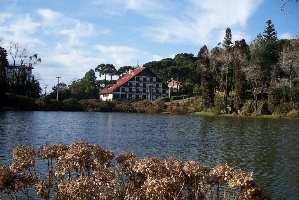 Um extenso lago cercado por árvores e construções em estilo europeia para representar airbnb em Gramado