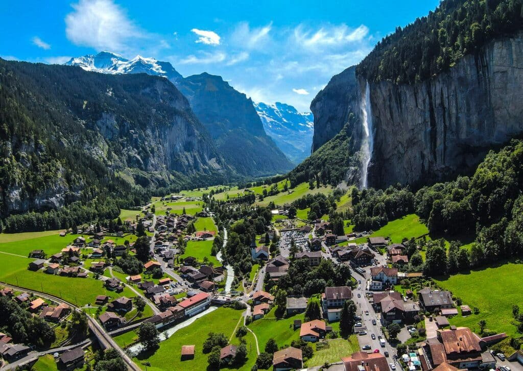 Imagem da cidade de Lauterbrunnen, Suíça durante o dia com a cidade a frente em volta de arvores, montanhas e cachoeiras.