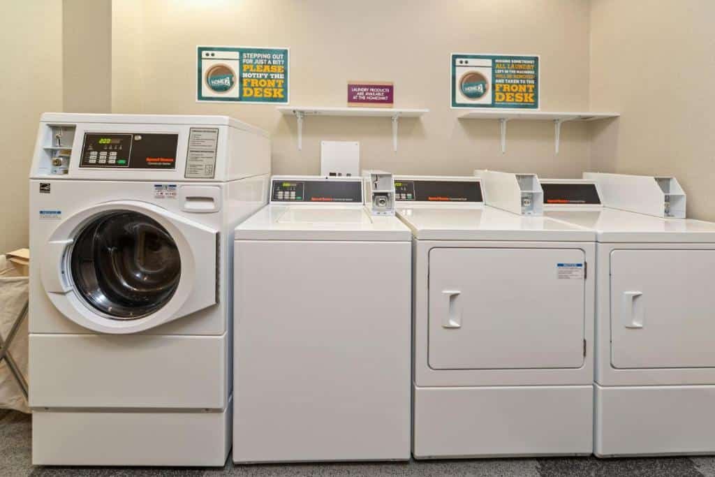 Imagem de uma lavanderia no Home2 Suites Newark Airport. O espaço é equipado com lavadoras e secadoras de roupas para uso dos hóspedes. Há também uma bancada de trabalho, onde é possível dobrar e organizar as roupas. O ambiente é funcional e oferece conveniência aos visitantes. O Home2 Suites Newark Airport é um dos hotéis perto do aeroporto de Newark.