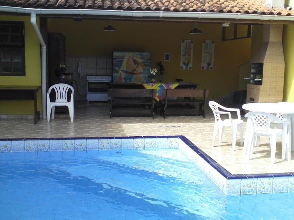 Piscina ao ar livre do Makitub. Atrás da piscina o rancho da hospedagem, com churrasqueira, mesas, cadeiras, fogão e pia.