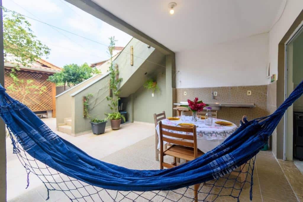 Área de lazer da Pousada Movimenthai. Uma rede azul, uma mesa com quatro cadeiras e um quintal aberto com plantas. Foto para ilustrar post sobre Pousadas em Boracéia.