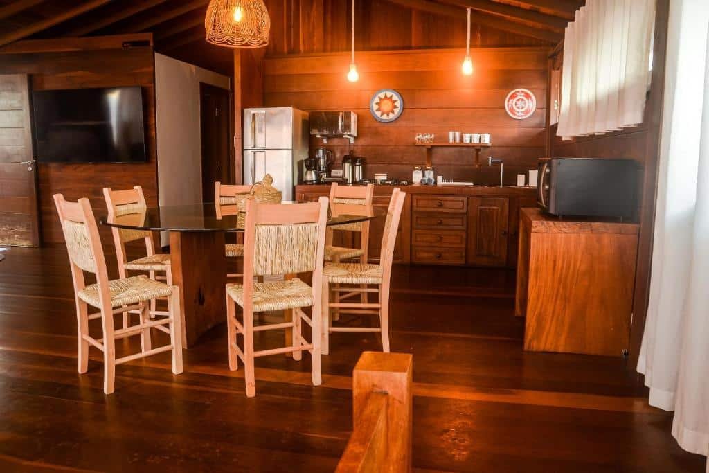 Cozinha do Local Brasil House. Uma mesa de vidro com cadeiras no meio, no fundo a cozinha toda equipada, do lado esquerdo uma televisão.
