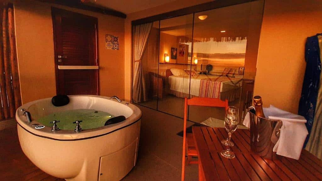 Vista do quarto com o entardecer. Uma banheira de hidromassagem na varanda com uma mesa e vinho. No fundo o quarto. Foto para ilustrar post sobre airbnb em Morro de São Paulo.