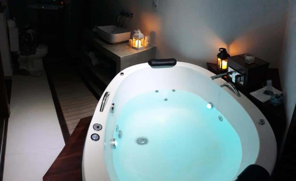 Banheira de hidromassagem da Novissima Casa. Uma banheira com luminárias ao redor, no fundo o vaso sanitário e a pia.