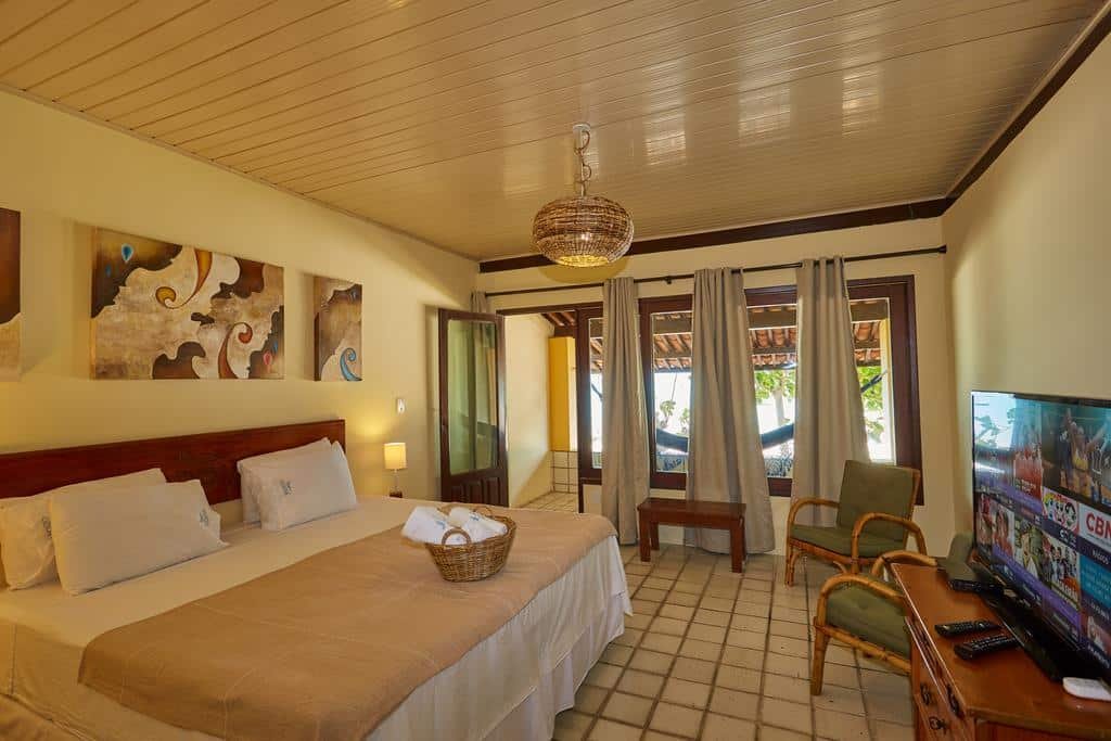 Quarto da Odoiá Maragogi Restaurante e Estalagem, com cama de casal, TV, duas poltronas verdes e uma varanda com rede
